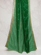 Bottle-green net dupatta with sequin embellishments and gold thread embroidered border set against white marble background by Ladylike Accoutre. 