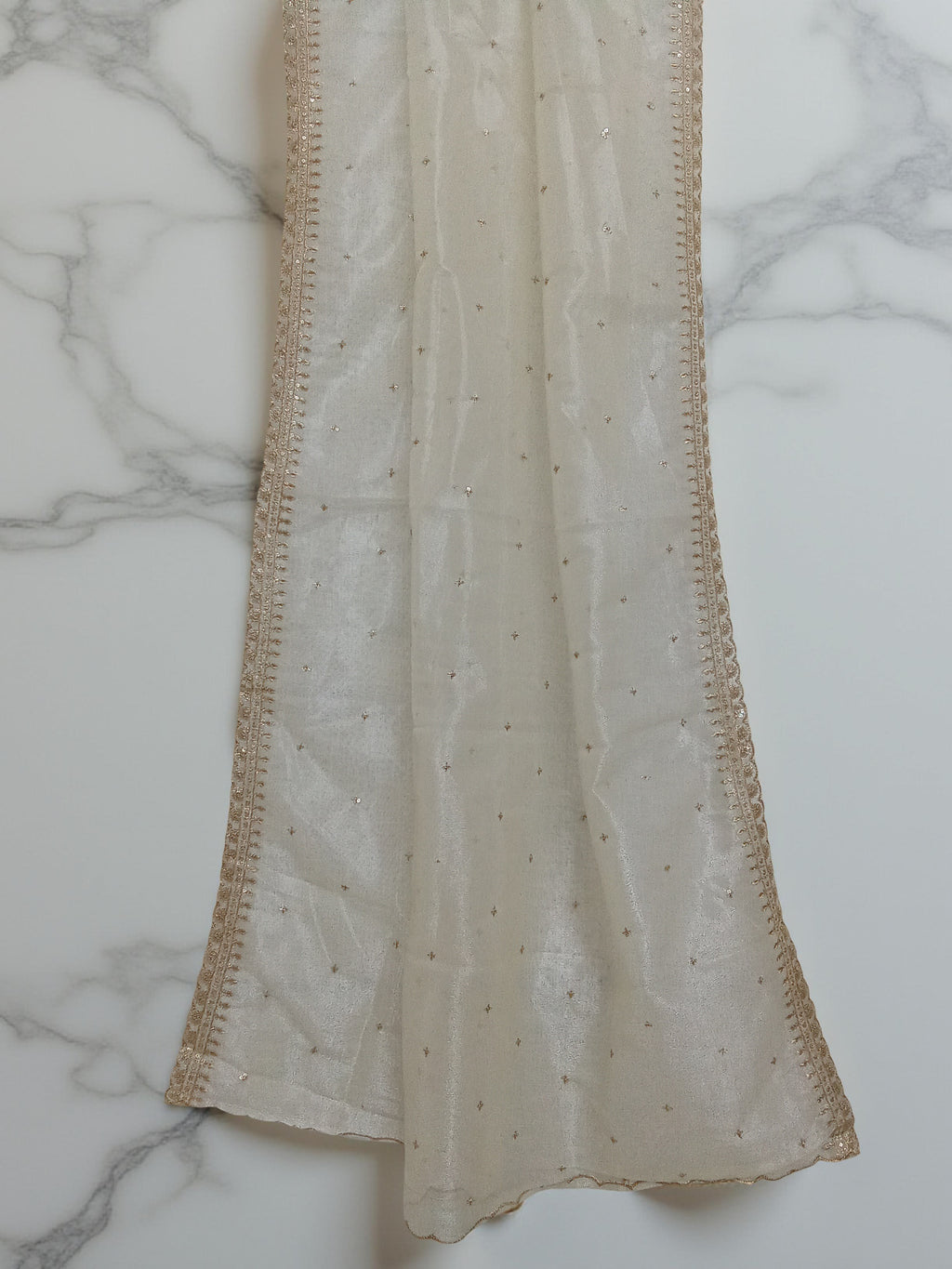 Cream net dupatta with sequin embellishments and gold thread embroidered border set against a  white marble background by Ladylike Accoutre. 