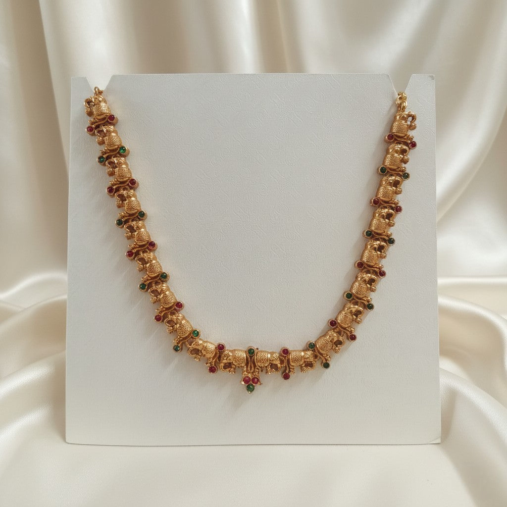 Gold-Tone Elephant Motif Necklace with Red & Green Stone Accents and adjustable dori set on a cream shining background by Ladylike Accoutre