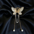 Gold-Tone butterfly hair claw clip with white crystals and dangling pearl tassel chains on a dark satin fabric background. Crated by Ladylike Accoutre