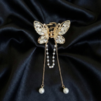 Gold-Tone butterfly hair claw clip with white crystals and dangling pearl tassel chains on a dark satin fabric background. Crated by Ladylike Accoutre