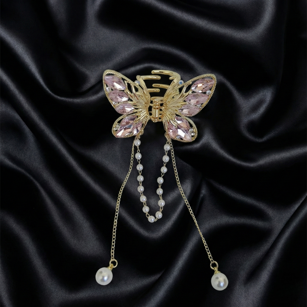 Gold-Tone butterfly hair claw clip with pink crystals and dangling pearl tassel chains on a dark satin fabric background. Crated by Ladylike Accoutre