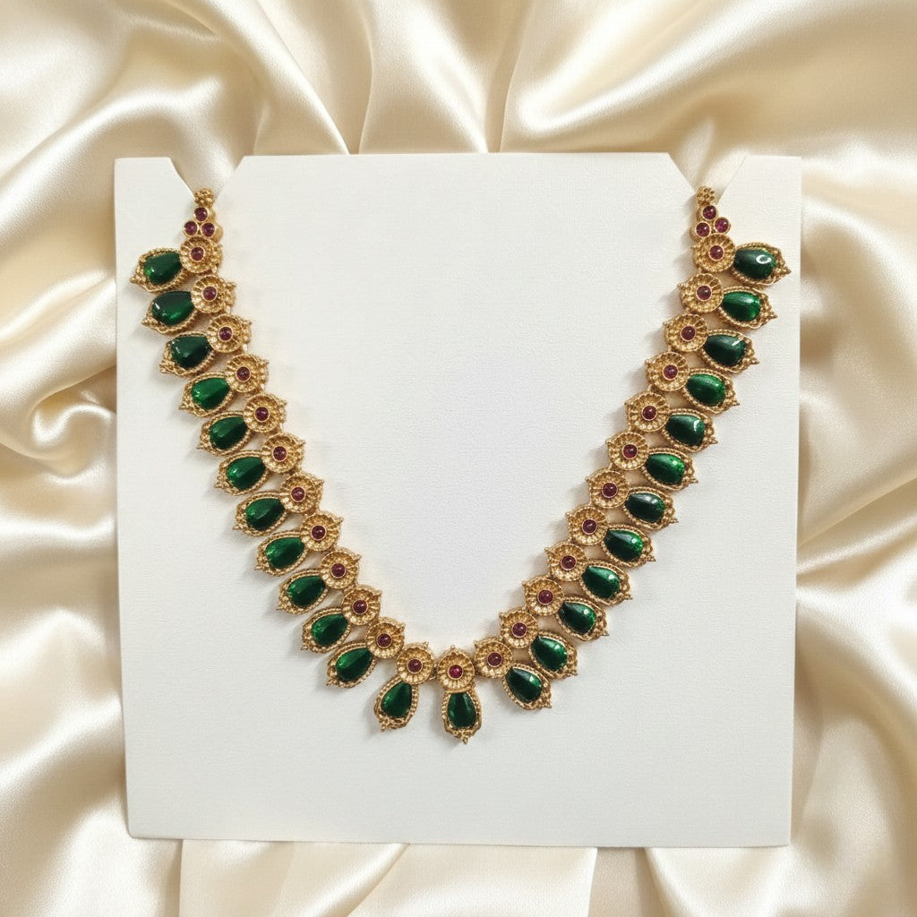 Palakka Mala Necklace Set with Emerald-Green Leaf Stones & Ruby-Red Accents and adjustable dori set on a cream shining background by Ladylike Accoutre