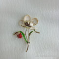 Gold-tone flower brooch featuring cream enamel petals and a sparkling crystal center. A vibrant green leaf branches off the stem, supporting a small, detailed red ladybug.