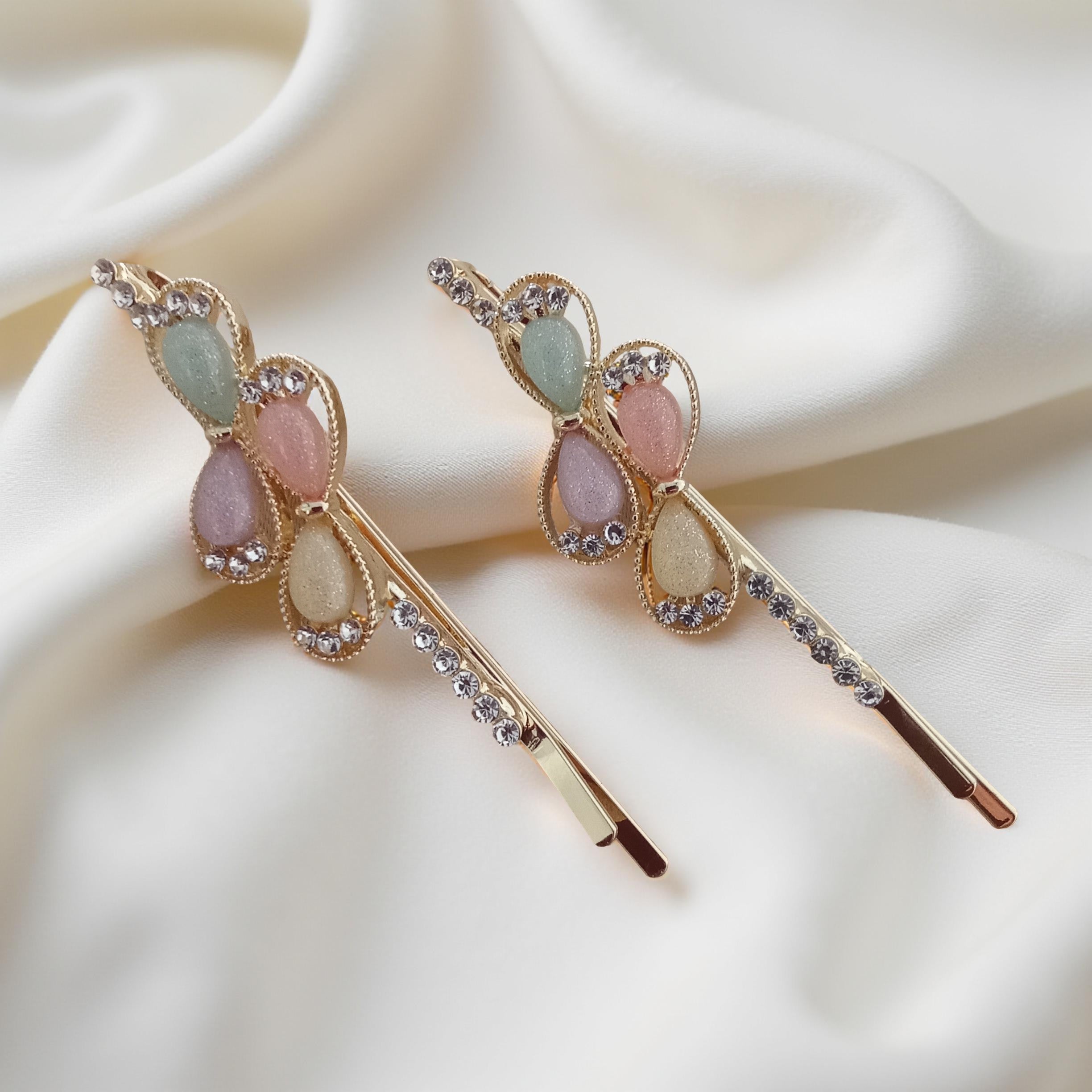 Pair of gold-tone hair pins featuring multi-colored teardrop stones and clear crystal accents. Teardrop gems are framed by twisted gold borders. Curated by Ladylike Accoutre