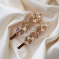 Pair of gold-tone butterfly hair pins featuring faceted peach teardrop stones and pave crystals. Fancy hair slide for women displayed on a white silk background. Curated by Ladylike Accoutre.