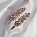 Pair of gold-tone butterfly hair pins featuring faceted multi-colored teardrop stones and pave crystals. Fancy hair slide for women displayed on a white silk background. Curated by Ladylike Accoutre.