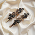 Pair of gold-tone butterfly hair pins featuring faceted black teardrop stones and pave crystals. Fancy hair slide for women displayed on a white silk background. Curated by Ladylike Accoutre.