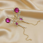 Large gold butterfly hair claw clip featuring magenta crystals and dangling gold chains with white faux pearls, set against a soft gold fabric background by Ladylike Accoutre