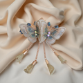 Twin embroidered butterflies in cream color on a rose gold-tone barrette hair clip with crystal accents and mesh charms, set against a soft cream background. Curated by Ladylike Accoutre.