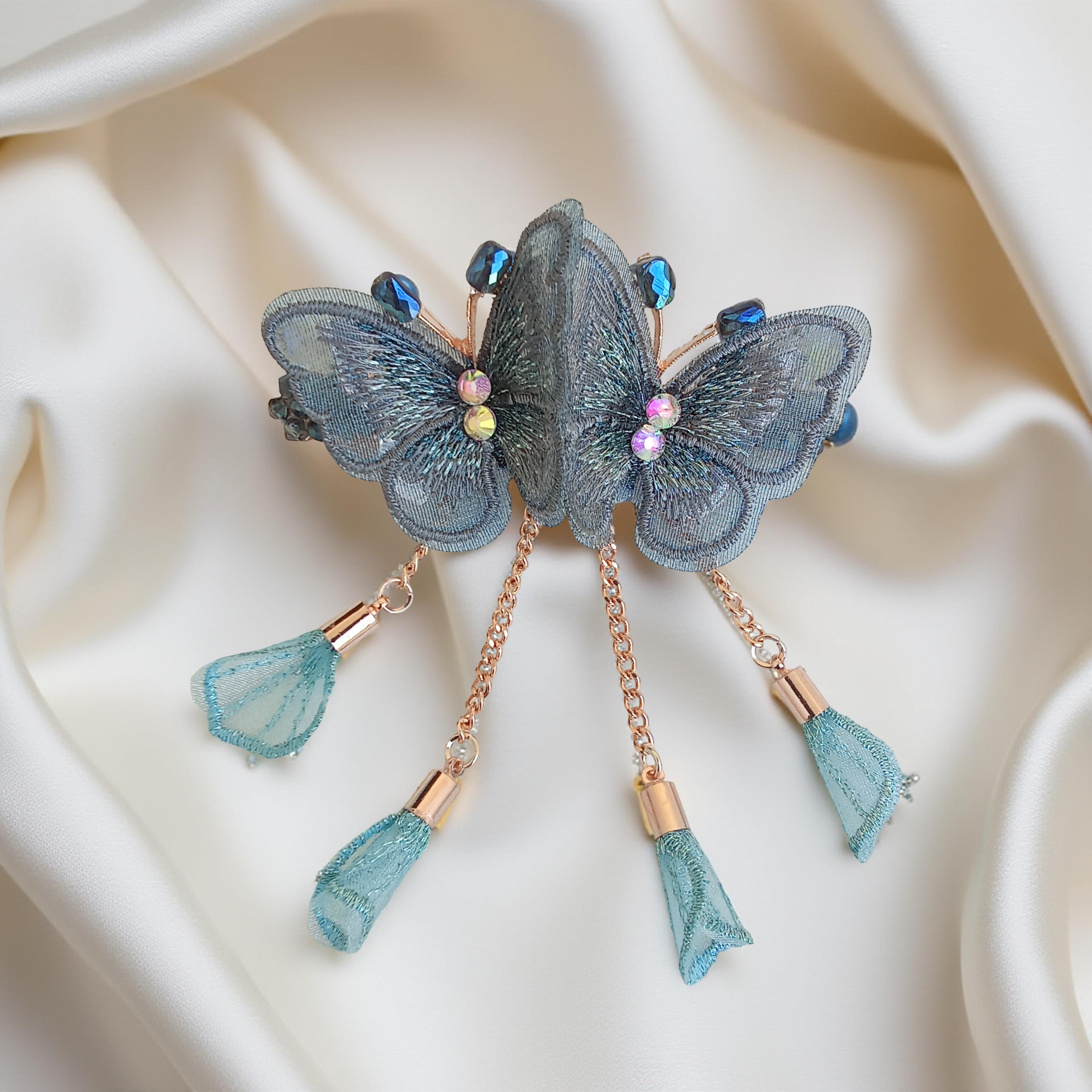 Twin embroidered butterflies in blue grey color on a rose gold-tone barrette hair clip with crystal accents and mesh charms, set against a soft white background. Curated by Ladylike Accoutre.