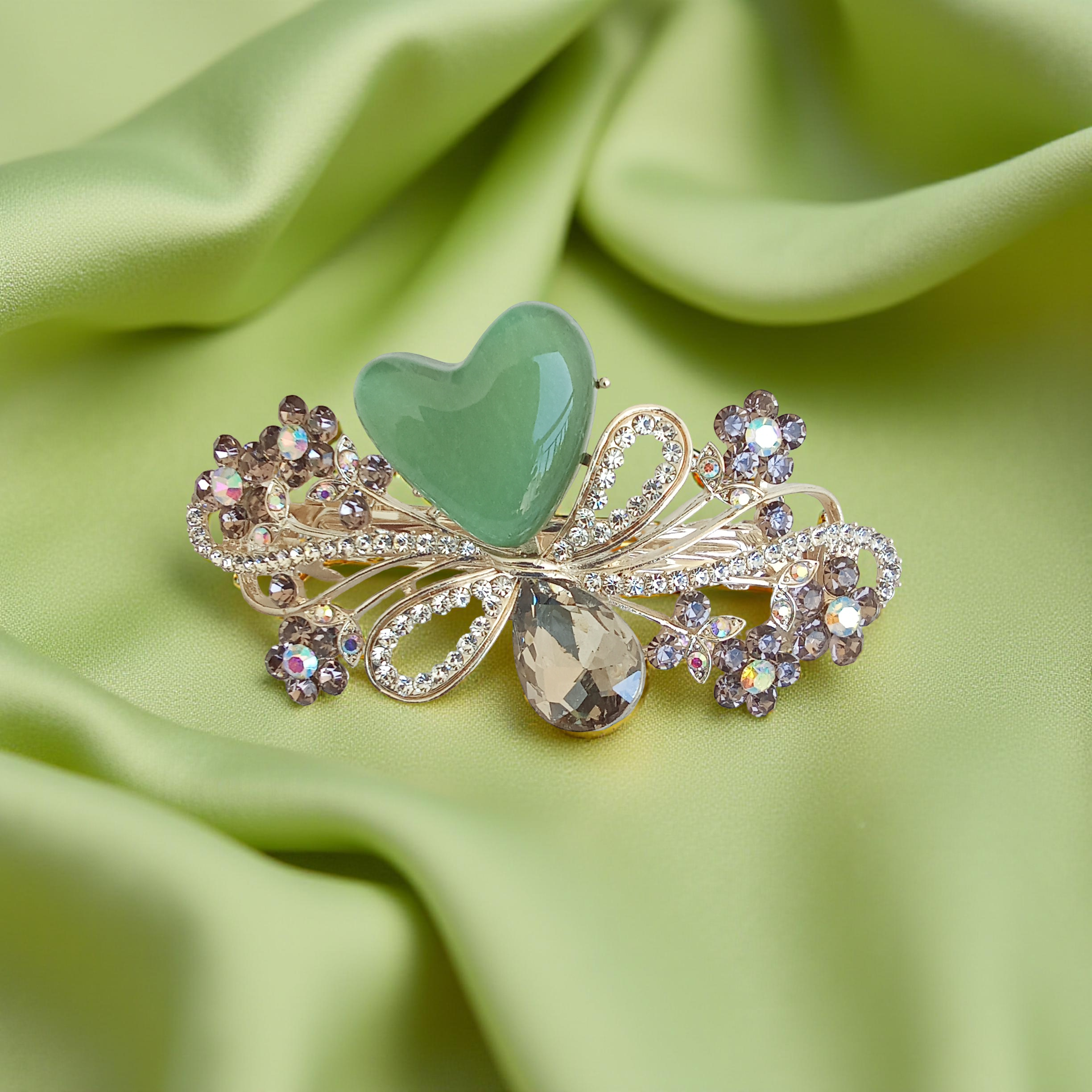 Ornate gold-tone floral barrette hair clip with a jade green stone, crystal-encrusted flowers, and a smoky teardrop gem, displayed on a silky off-green fabric background. Curated by Ladylike Accoutre.
