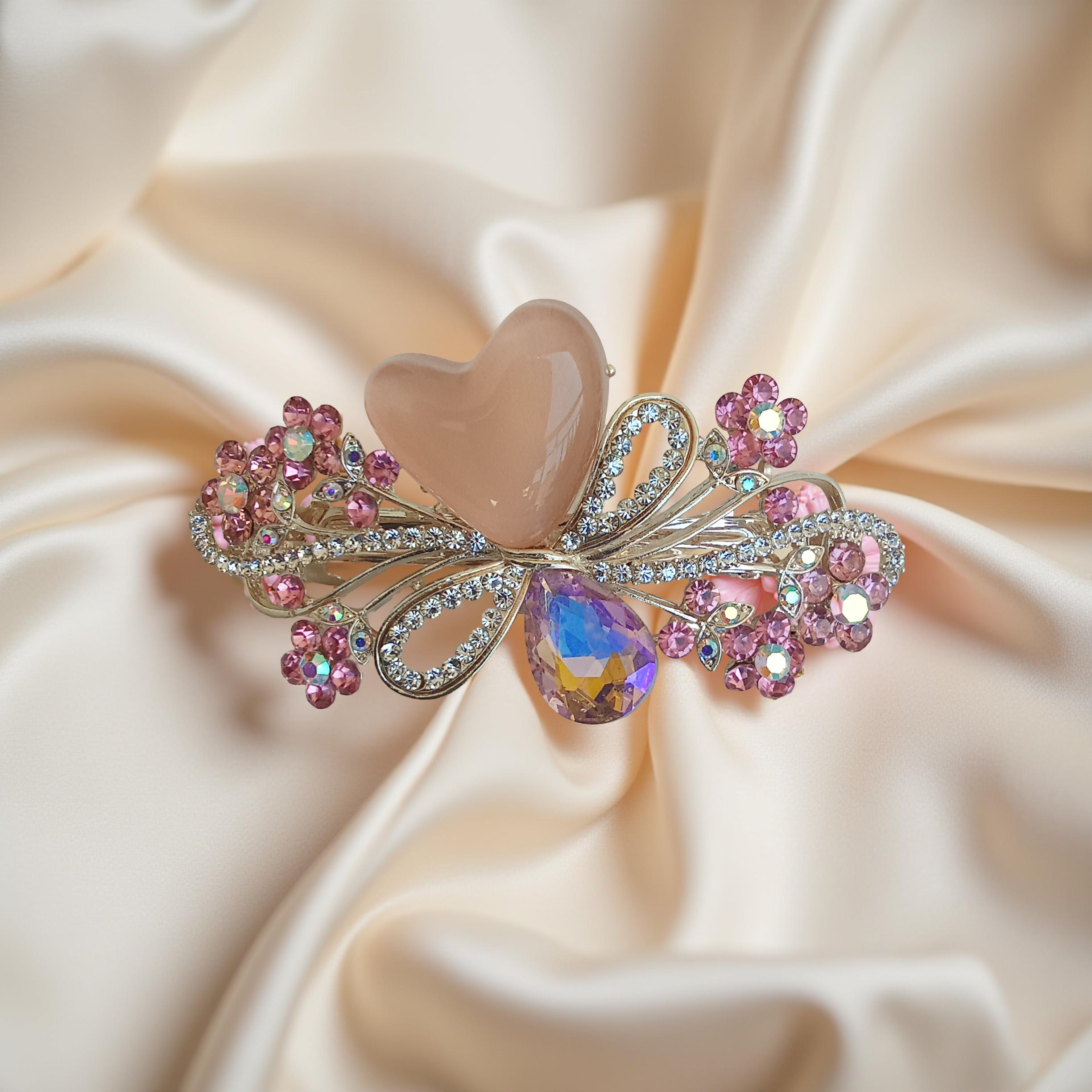 Ornate gold-tone floral barrette hair clip with a peach heart stone, pink crystal-encrusted flowers and a smoky teardrop gem, displayed on a silky pastel peach fabric background. Curated by Ladylike Accoutre.
