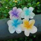 Plumeria Flower Hair Claw Clip, Set of 4 Clips on a metal rod with green foliage in the background. Featuring tropical gradient designs in Purple, Blue, Green and Yellow. Curated by Ladylike Accoutre.
