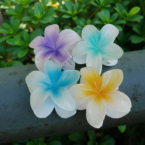 Plumeria Flower Hair Claw Clip, Set of 4 Clips on a metal rod with green foliage in the background. Featuring tropical gradient designs in Purple, Blue, Green and Yellow. Curated by Ladylike Accoutre.