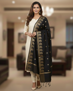 A model in cream salwar kameez wearing a Banarasi-inspired Black Art Silk Dupatta with Tassels by Ladylike Accoutre, displayed on a clean white background. Features gold zari butti floral motifs and an intricate paisley border.