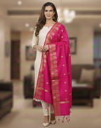 A model in cream salwar kameez wearing a Banarasi-inspired Rani Pink Art Silk Dupatta with Tassels by Ladylike Accoutre, displayed on a clean white background. Features gold zari butti floral motifs and an intricate paisley border.
