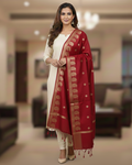 A model in cream salwar kameez wearing a Banarasi-inspired Ruby Red Art Silk Dupatta with Tassels by Ladylike Accoutre, displayed on a clean white background. Features gold zari butti floral motifs and an intricate paisley border.