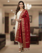 A model in cream salwar kameez wearing a Banarasi-inspired Ruby Red Art Silk Dupatta with Tassels by Ladylike Accoutre, displayed on a clean white background. Features gold zari butti floral motifs and an intricate paisley border.