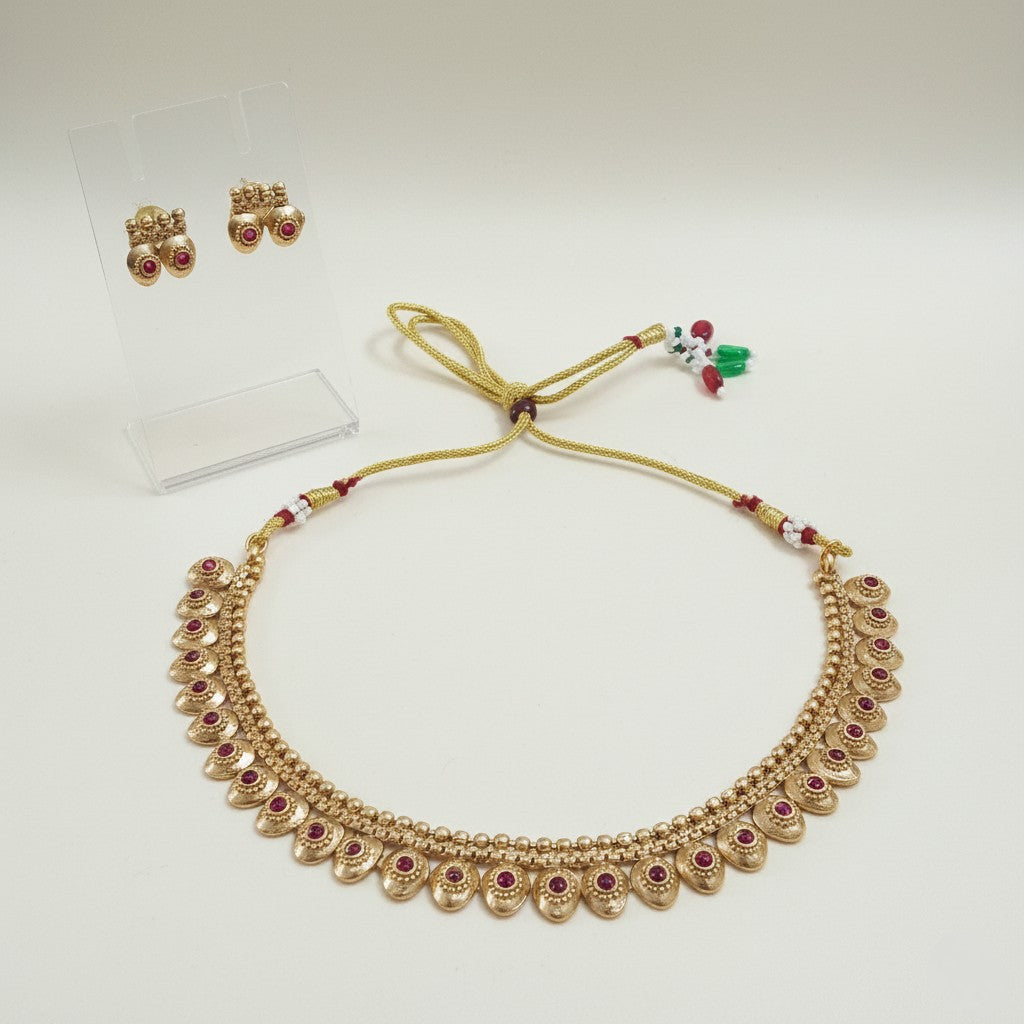 Gold-tone Mango Malai choker necklace set with ruby-red kemp stones, adjustable dori, and matching stud earrings set on a plain clean white background by Ladylike Accoutre.