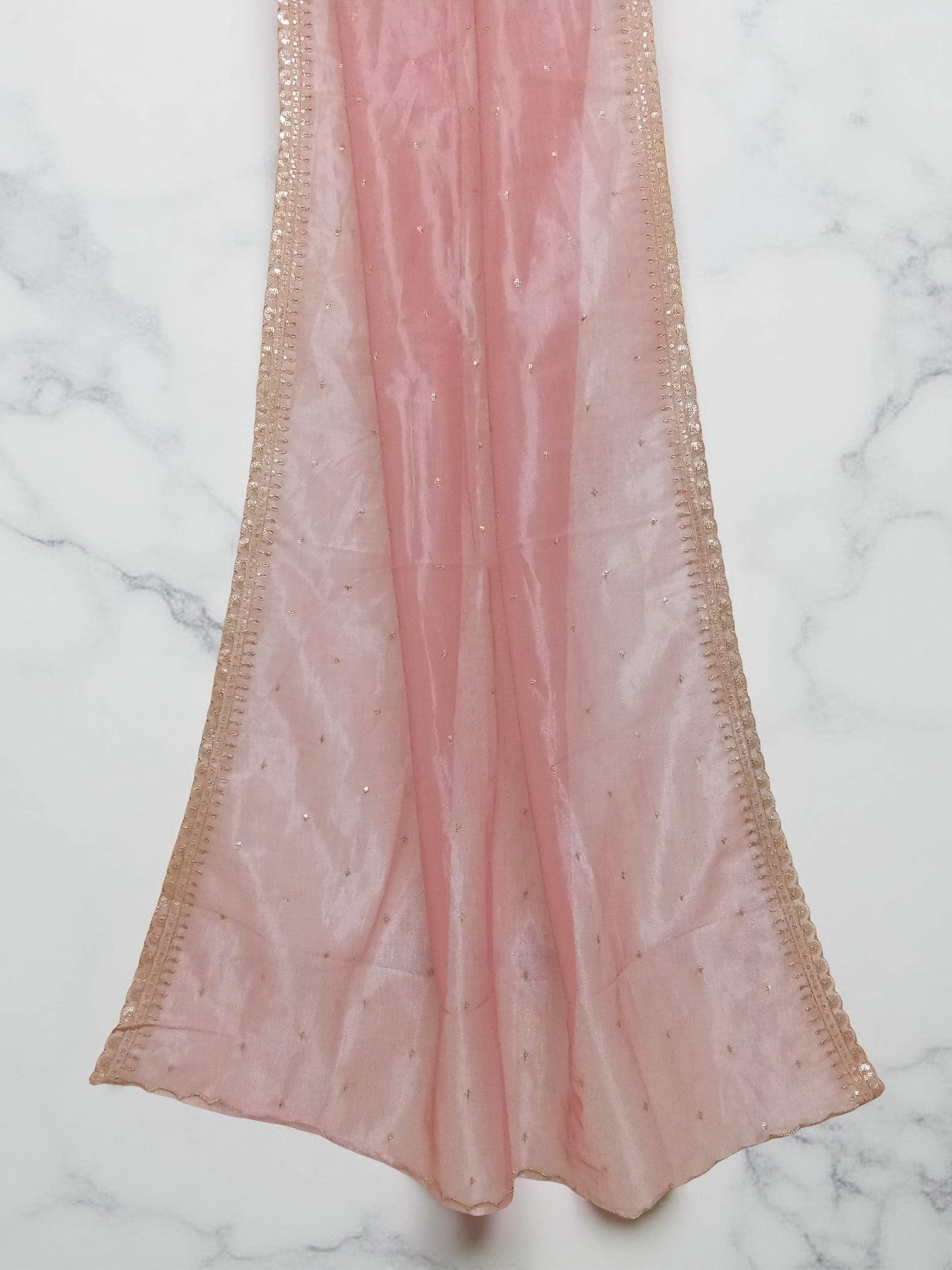 Peach net dupatta with sequin embellishments and gold thread embroidered border set against white marble background by Ladylike Accoutre. 