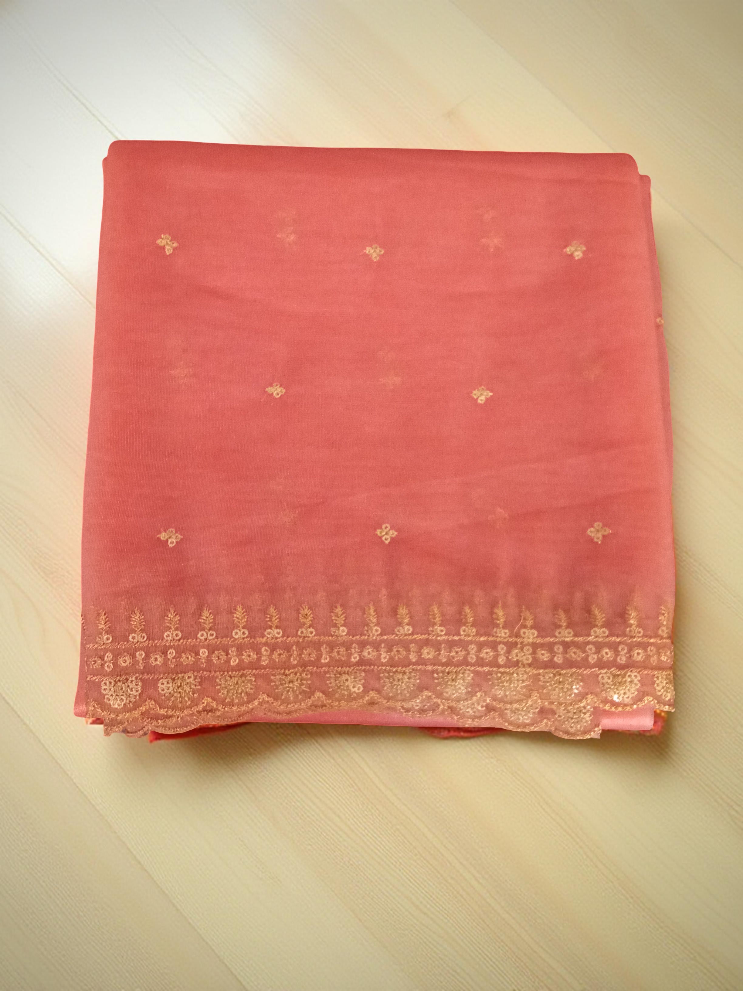 Peach net dupatta with sequin embellishments and gold thread embroidered border on a wooden floor by Ladylike Accoutre.