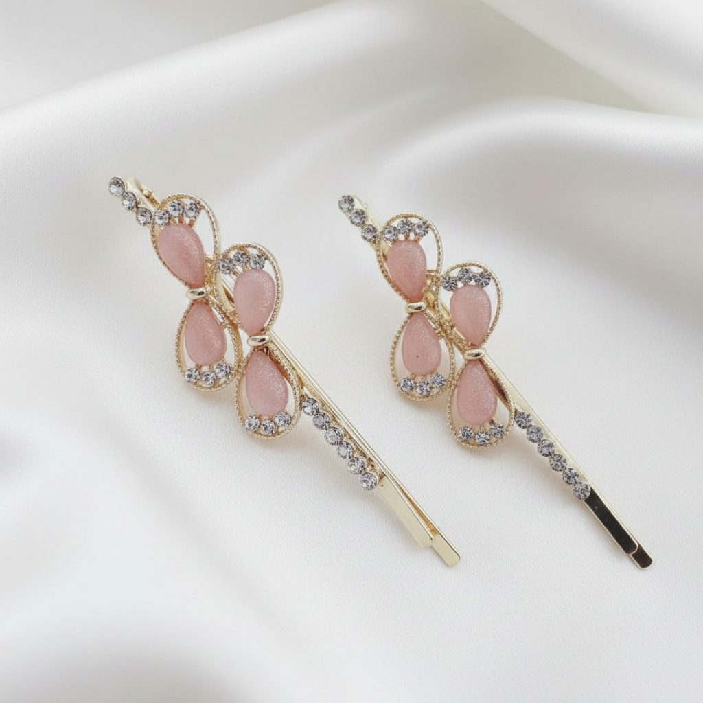 Pair of gold-tone hair pins featuring pink teardrop stones and clear crystal accents. Teardrop gems are framed by twisted gold borders. Curated by Ladylike Accoutre