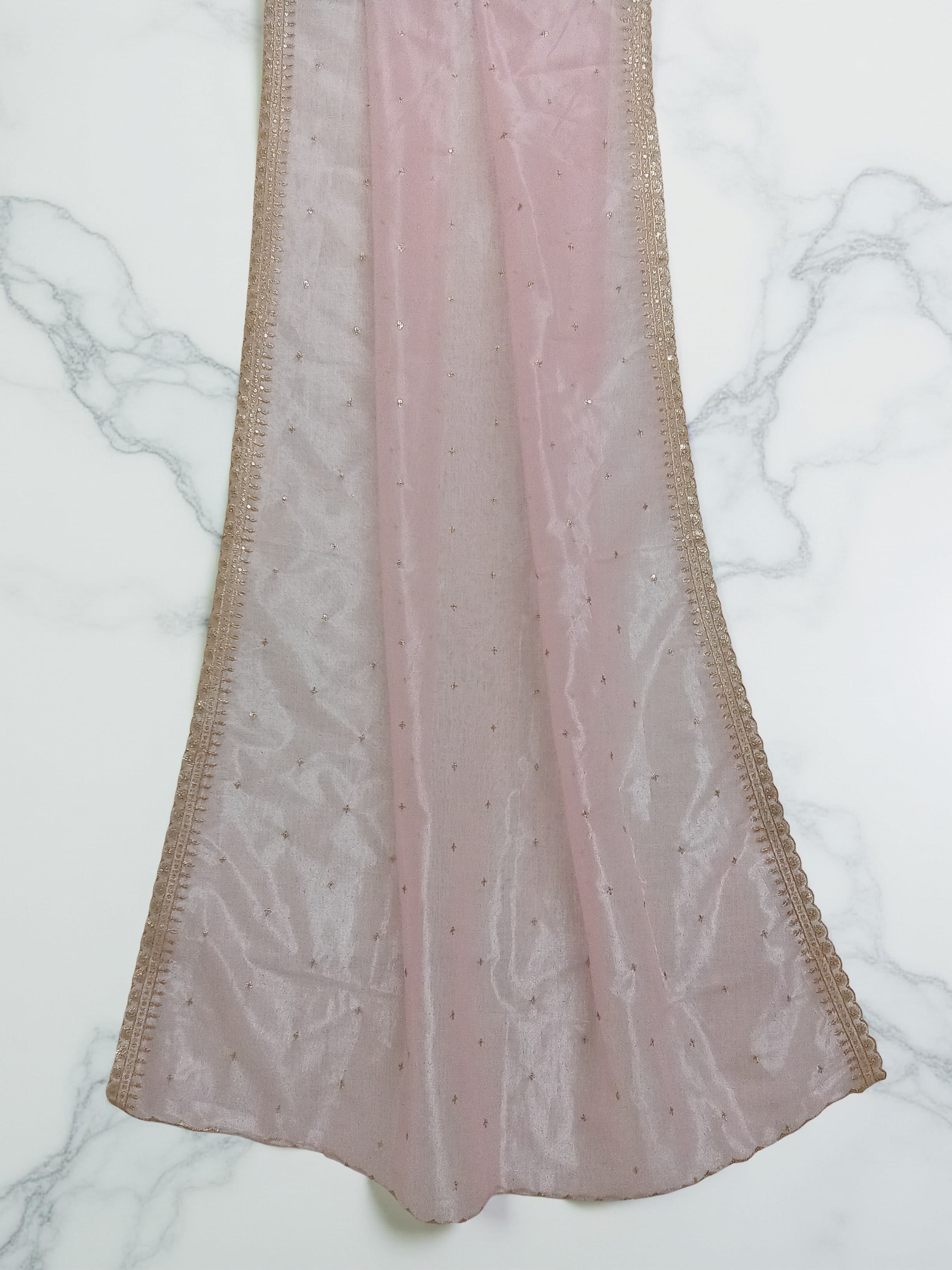 Pink net dupatta with sequin embellishments and gold thread embroidered border set against white marble background by Ladylike Accoutre. 