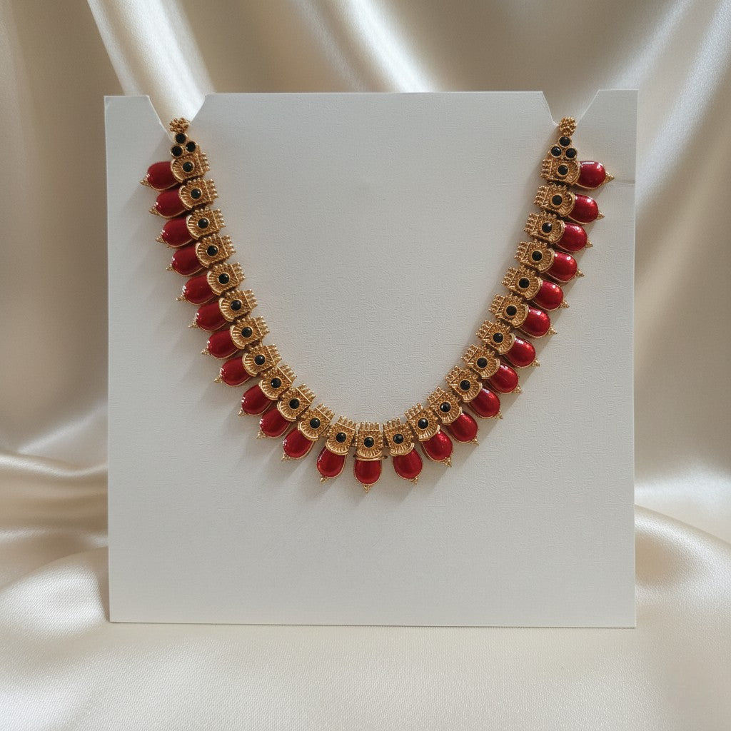 Red Palakka Mala Necklace with Emerald-Green Leaf Accents and adjustable dori set on a cream shining background by Ladylike Accoutre