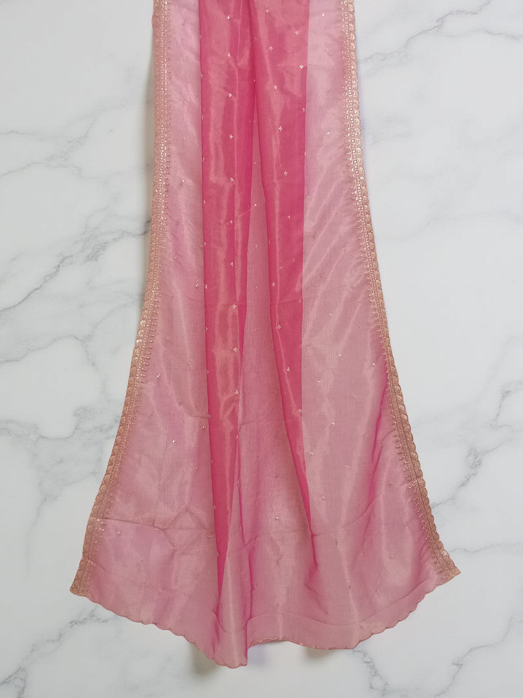 Reddish-Pink net dupatta with sequin embellishments and gold thread embroidered border set against white marble background by Ladylike Accoutre. 