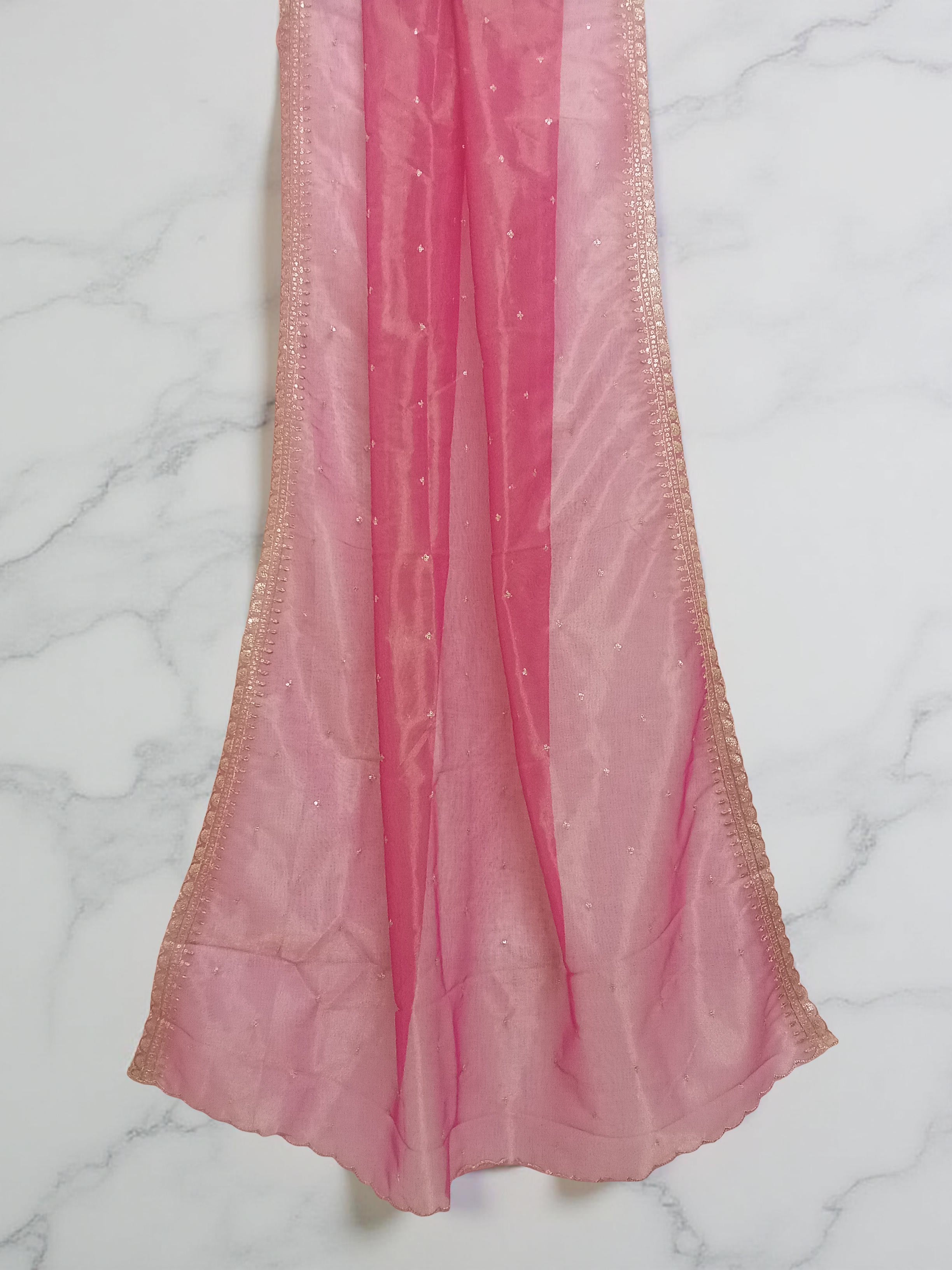 Reddish-Pink net dupatta with sequin embellishments and gold thread embroidered border set against white marble background by Ladylike Accoutre. 