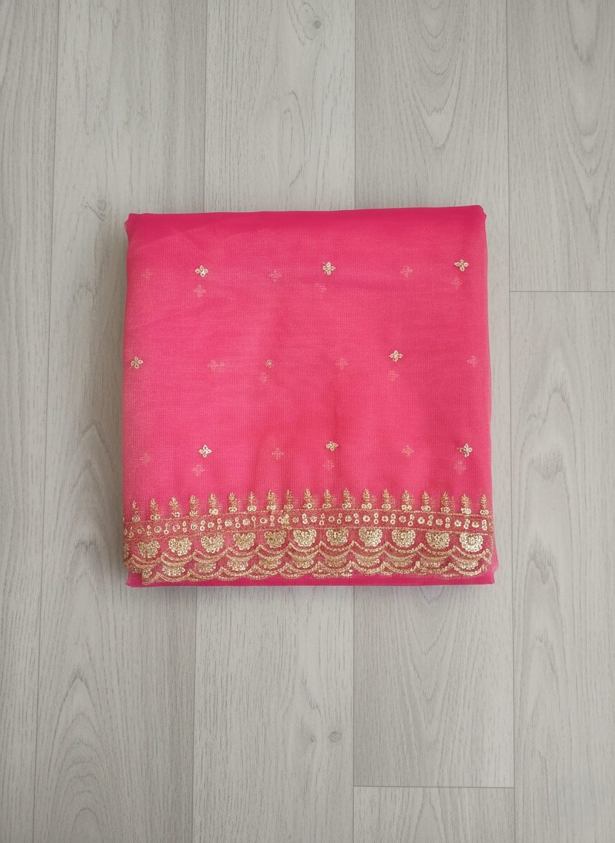 Reddish-Pink net dupatta with sequin embellishments and gold thread embroidered border on a wooden floor by Ladylike Accoutre.