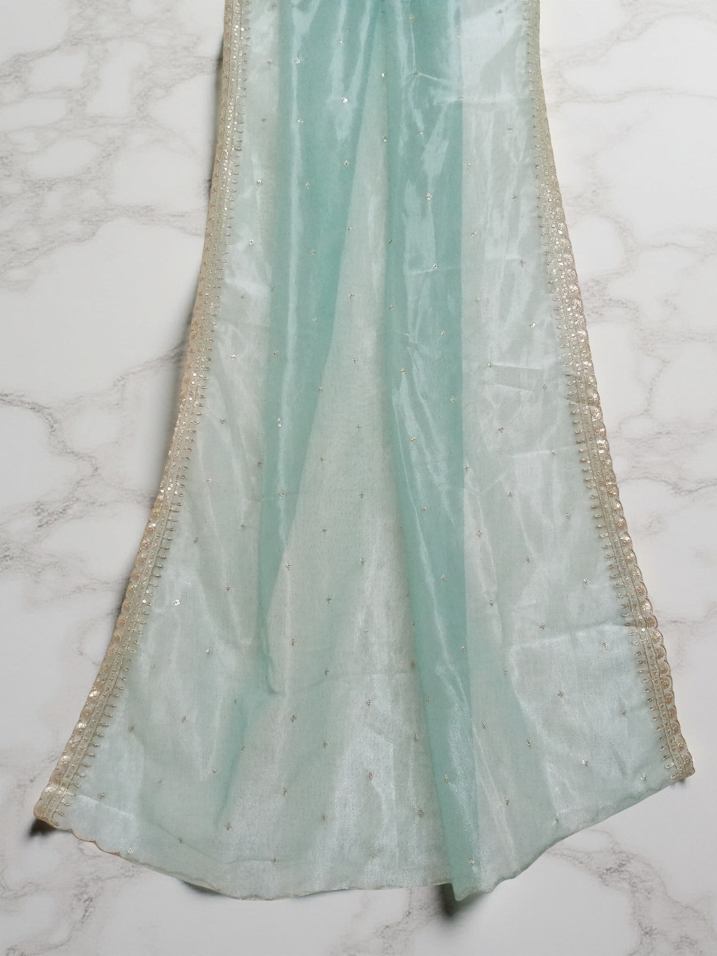Sea-Green net dupatta with sequin embellishments and gold thread embroidered border set against white marble background by Ladylike Accoutre. 
