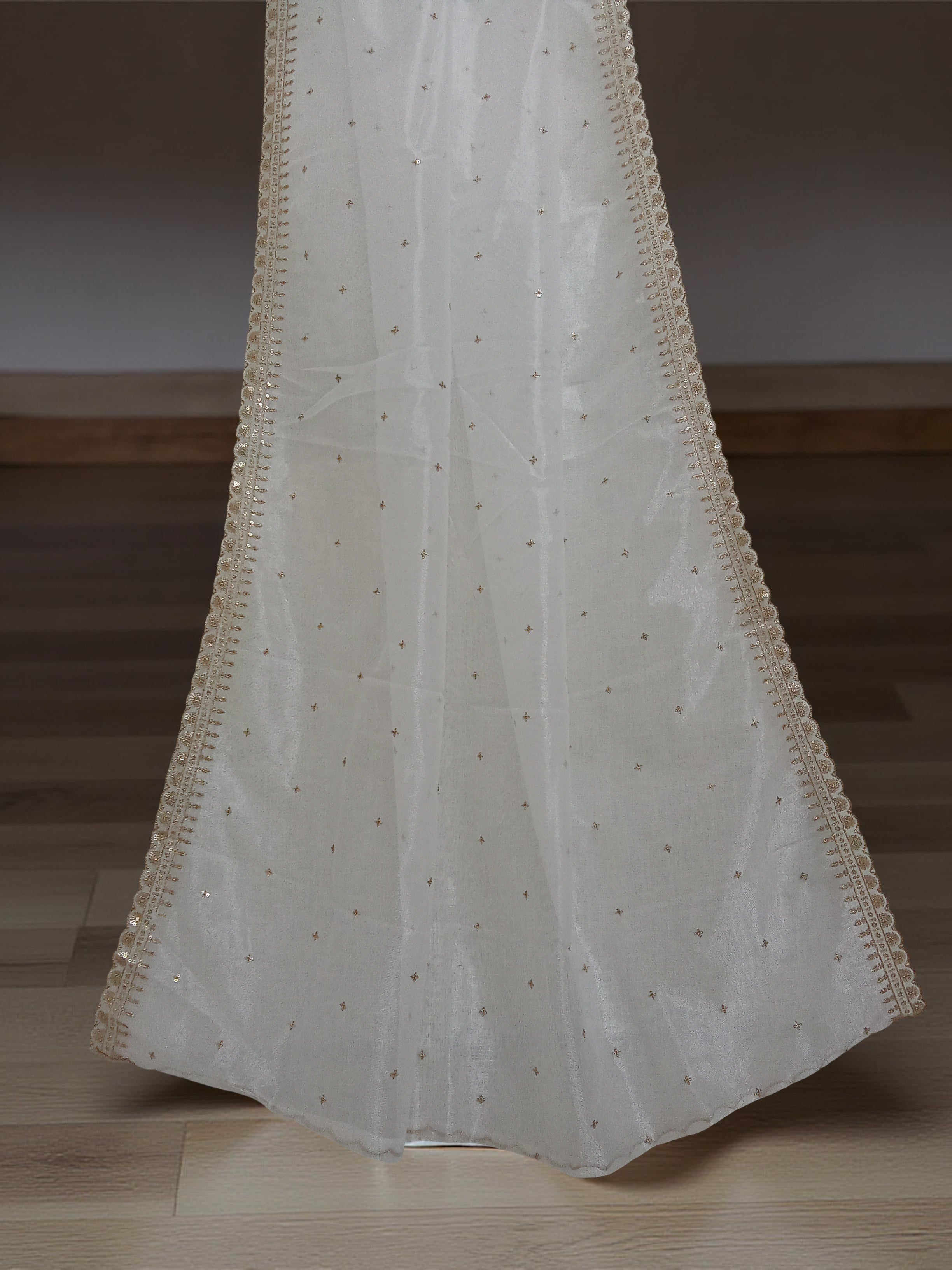 White net dupatta with sequin embellishments and gold thread embroidered border set against a wooden floor and white wall background by Ladylike Accoutre. 