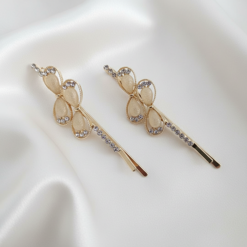 Pair of gold-tone hair pins featuring cream teardrop stones and clear crystal accents. Teardrop gems are framed by twisted gold borders. Curated by Ladylike Accoutre